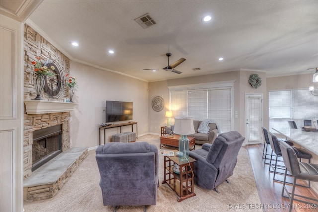 living room featuring a stone fireplace, ornamental molding, light hardwood / wood-style floors, and ceiling fan