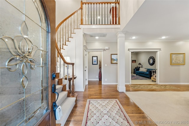 entryway with hardwood / wood-style flooring, ornamental molding, a high ceiling, and ornate columns