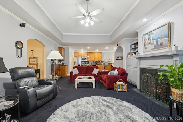 living room featuring crown molding, ceiling fan, a high end fireplace, built in shelves, and dark carpet