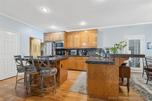 kitchen with a kitchen bar, crown molding, appliances with stainless steel finishes, kitchen peninsula, and decorative backsplash