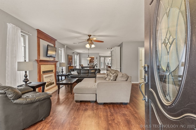 living room featuring ceiling fan, dark hardwood / wood-style flooring, and a tiled fireplace