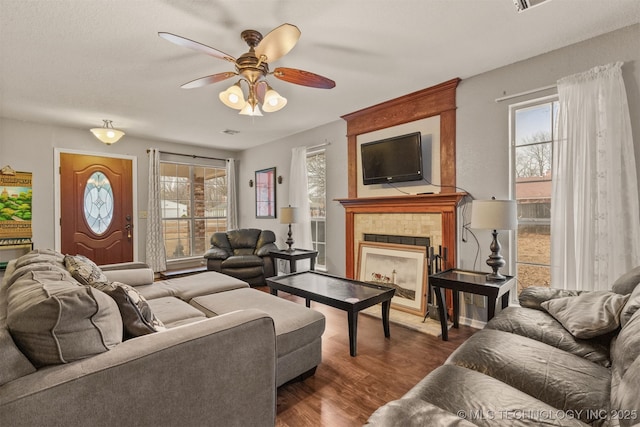 living room with a tiled fireplace, dark wood-type flooring, and ceiling fan