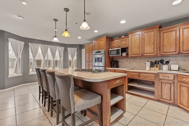 kitchen with hanging light fixtures, backsplash, stainless steel appliances, a center island, and light tile patterned flooring