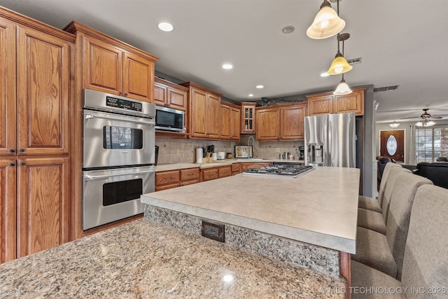 kitchen featuring a kitchen bar, sink, tasteful backsplash, decorative light fixtures, and stainless steel appliances