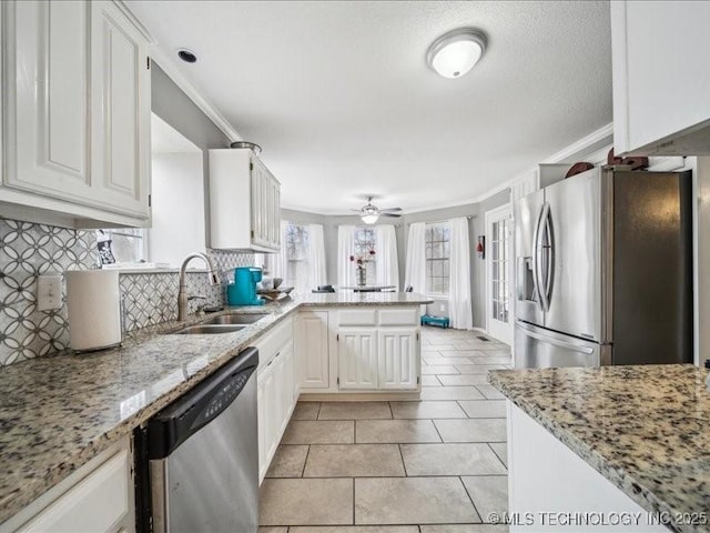 kitchen featuring appliances with stainless steel finishes, white cabinetry, sink, light stone counters, and kitchen peninsula