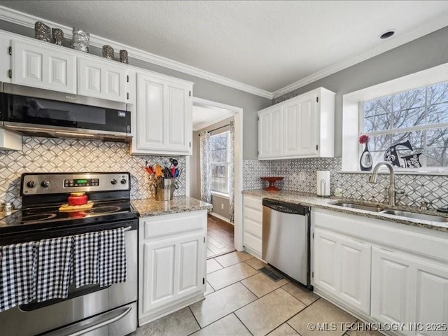 kitchen with sink, white cabinetry, stainless steel appliances, ornamental molding, and light stone countertops