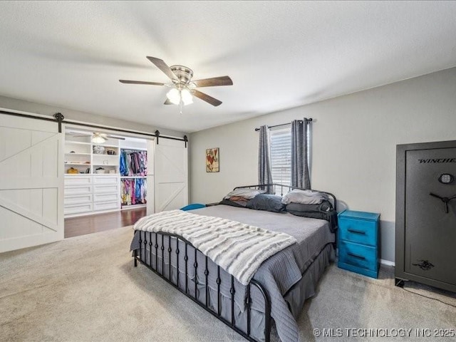 bedroom with ceiling fan, a barn door, and carpet floors