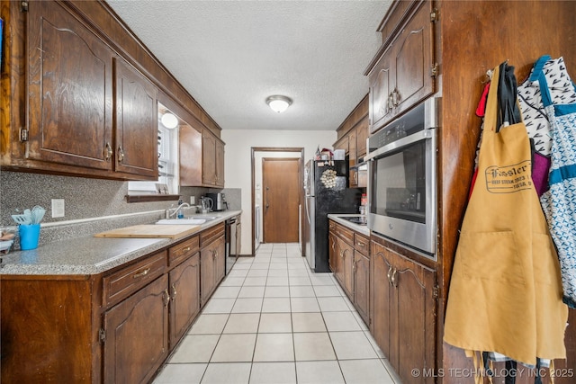 kitchen with light tile patterned floors, sink, stainless steel appliances, tasteful backsplash, and a textured ceiling