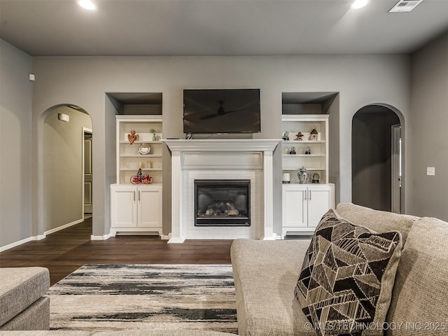 living room with a tiled fireplace, dark wood-type flooring, and built in features