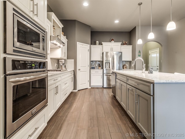 kitchen featuring a kitchen island with sink, decorative light fixtures, white cabinets, and appliances with stainless steel finishes