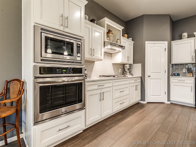 kitchen with light stone counters, stainless steel appliances, decorative backsplash, and white cabinets