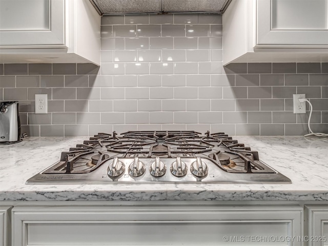 details featuring stainless steel gas cooktop, white cabinets, and light stone counters