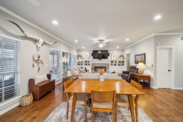 dining area with ornamental molding, a stone fireplace, hardwood / wood-style floors, and ceiling fan