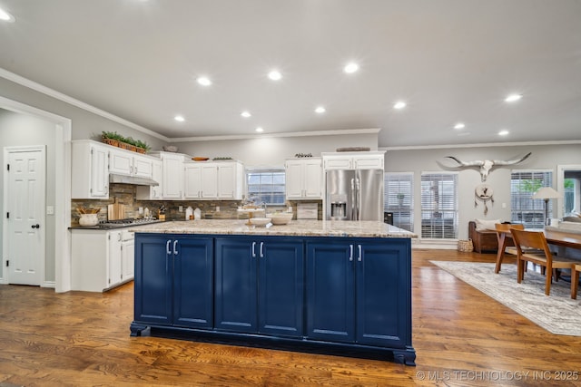 kitchen with dark wood-type flooring, appliances with stainless steel finishes, white cabinetry, light stone counters, and a kitchen island