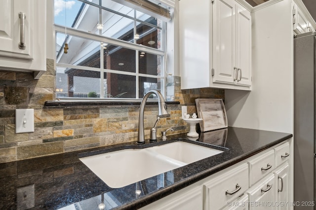 kitchen featuring sink, stainless steel fridge, dark stone countertops, backsplash, and white cabinets