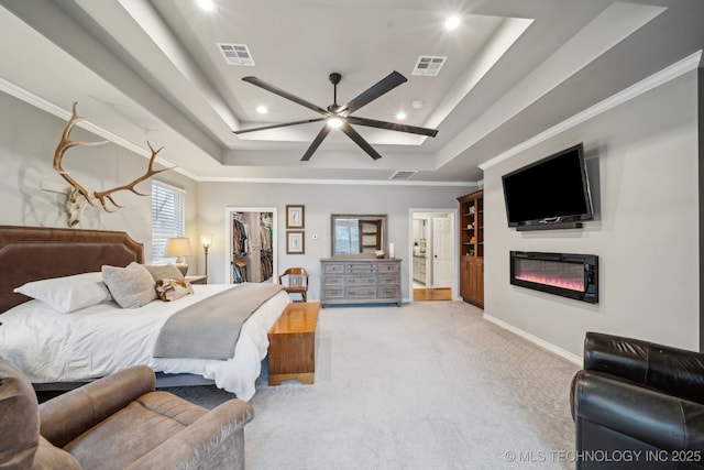 carpeted bedroom featuring ceiling fan, a walk in closet, a raised ceiling, and a closet