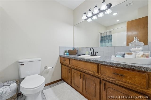 bathroom with tile patterned flooring, vanity, tasteful backsplash, toilet, and walk in shower