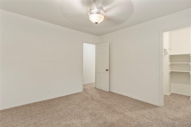 unfurnished bedroom featuring a walk in closet, light colored carpet, a closet, and ceiling fan