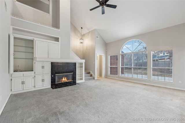 unfurnished living room with a tiled fireplace, ceiling fan, light carpet, and high vaulted ceiling