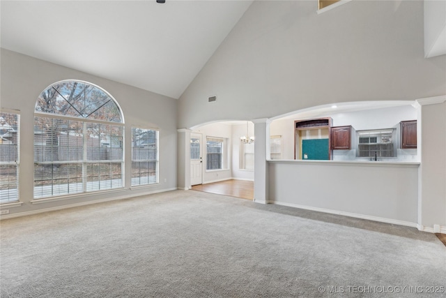 unfurnished living room featuring decorative columns, a chandelier, light carpet, and high vaulted ceiling