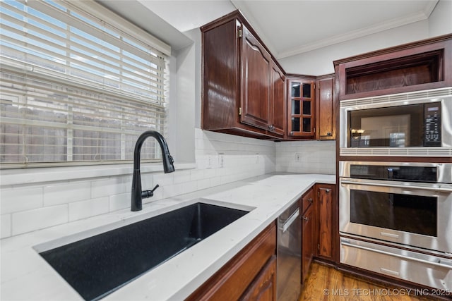 kitchen with appliances with stainless steel finishes, sink, decorative backsplash, ornamental molding, and dark wood-type flooring