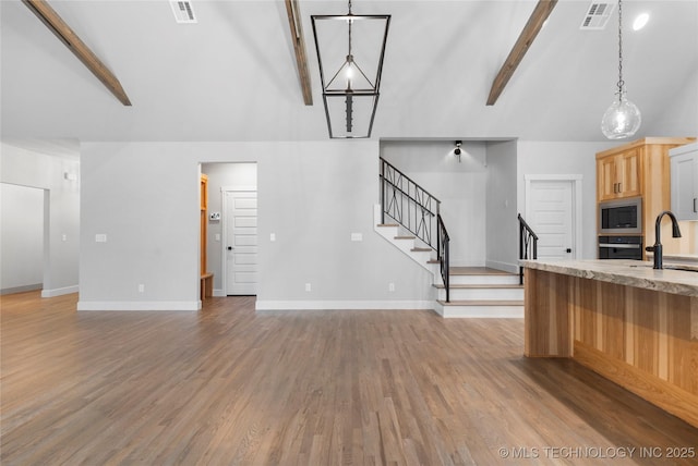 kitchen featuring pendant lighting, built in microwave, beamed ceiling, oven, and light hardwood / wood-style floors