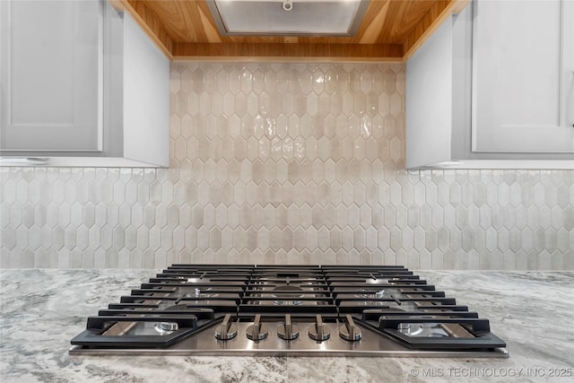 details featuring light stone counters, stainless steel gas stovetop, tasteful backsplash, and white cabinets