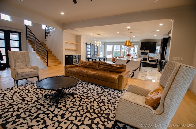 living room with ornamental molding, sink, an inviting chandelier, and light hardwood / wood-style floors