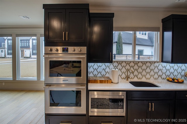 kitchen with appliances with stainless steel finishes, tasteful backsplash, sink, light hardwood / wood-style floors, and crown molding