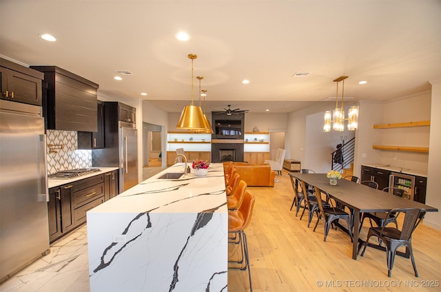 kitchen with pendant lighting, sink, appliances with stainless steel finishes, a large fireplace, and a center island with sink