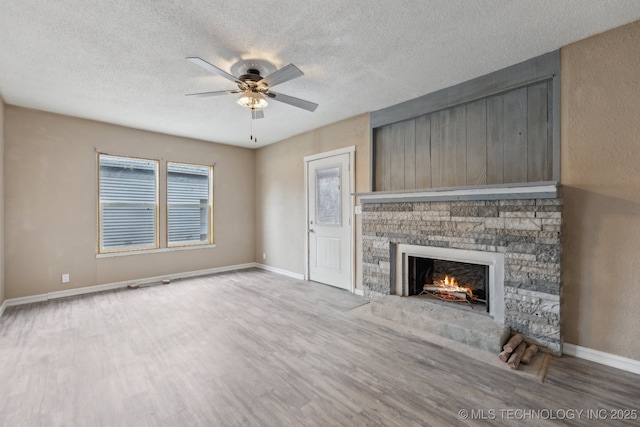 unfurnished living room with ceiling fan, a stone fireplace, light hardwood / wood-style floors, and a textured ceiling