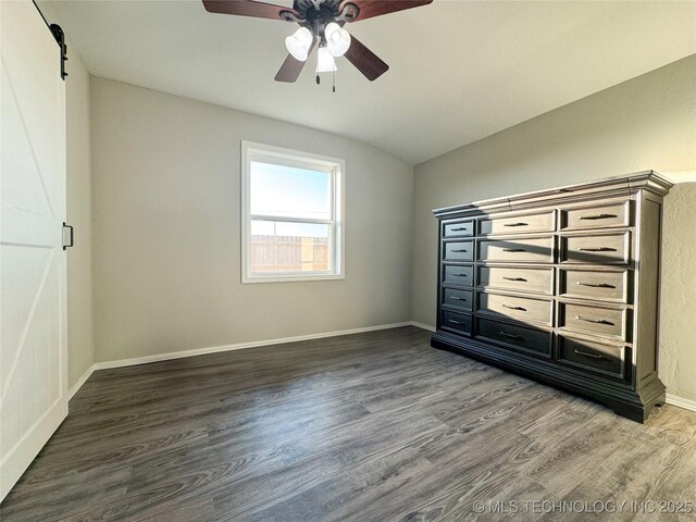 unfurnished bedroom with dark hardwood / wood-style flooring, lofted ceiling, a barn door, and ceiling fan