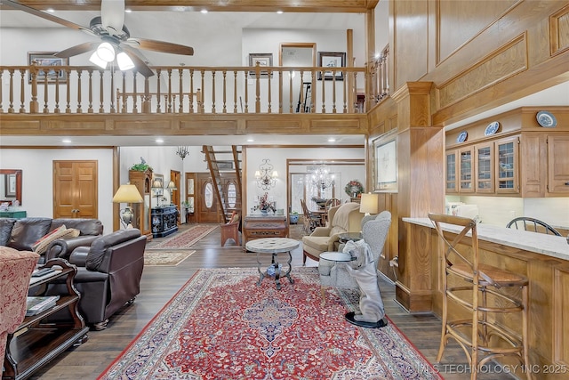 living room featuring dark hardwood / wood-style flooring, ceiling fan with notable chandelier, and a high ceiling