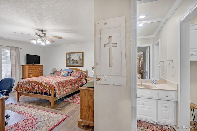 bedroom featuring connected bathroom, sink, ornamental molding, light hardwood / wood-style floors, and a textured ceiling