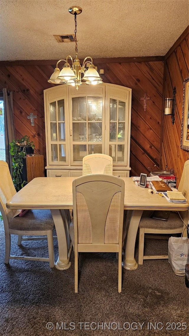 dining room with dark colored carpet, a chandelier, a textured ceiling, and wooden walls