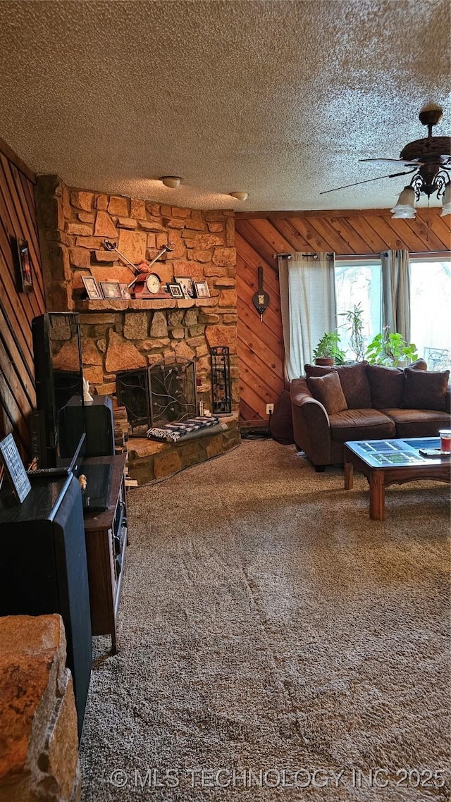 carpeted living room with ceiling fan, a fireplace, a textured ceiling, and wood walls