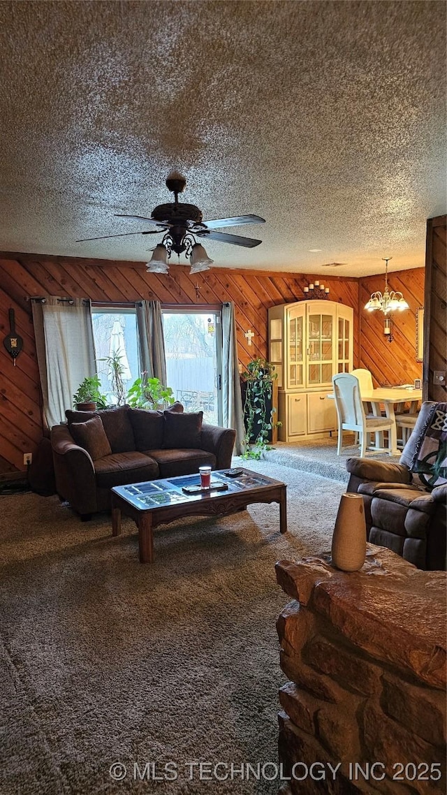 carpeted living room with ceiling fan with notable chandelier, wooden walls, and a textured ceiling