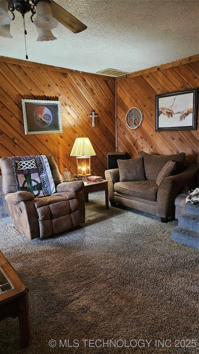 carpeted living room with ceiling fan, wooden walls, and a textured ceiling