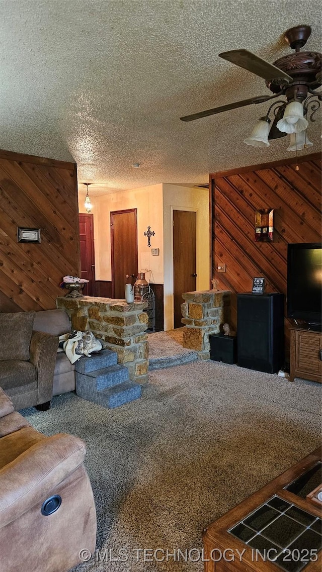 living room with ceiling fan, carpet flooring, a textured ceiling, and wood walls