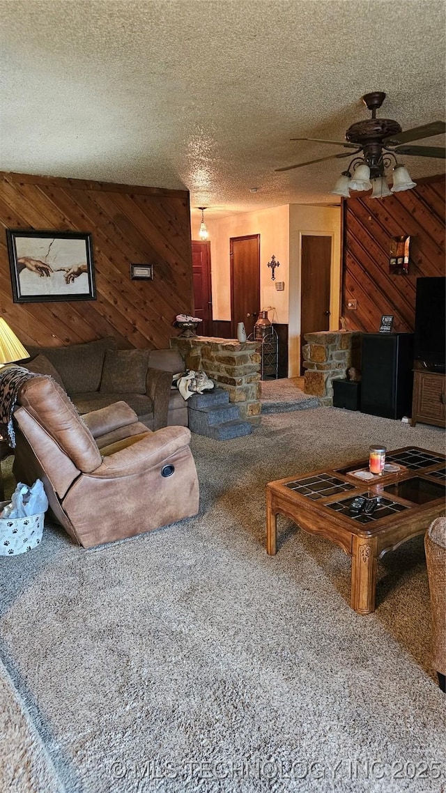 living room featuring ceiling fan, carpet flooring, a textured ceiling, and wooden walls