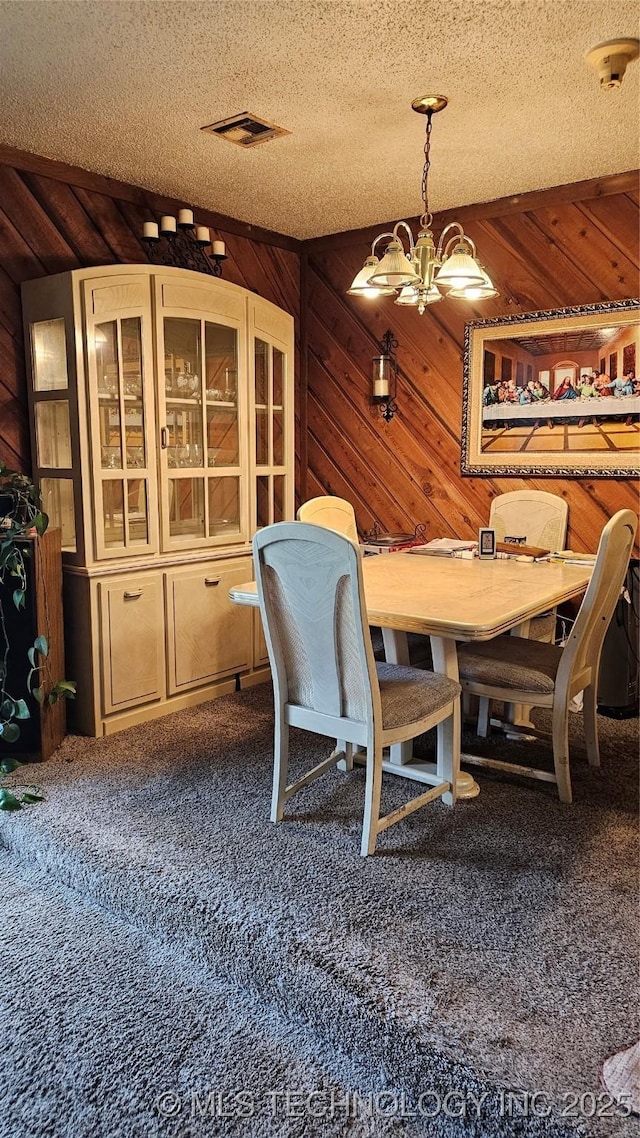 carpeted dining area with a textured ceiling, a notable chandelier, and wooden walls