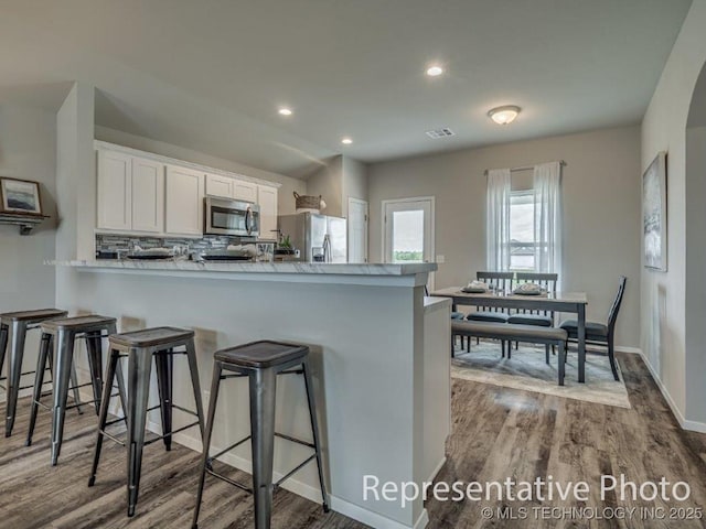 kitchen with appliances with stainless steel finishes, wood-type flooring, white cabinets, a kitchen bar, and kitchen peninsula