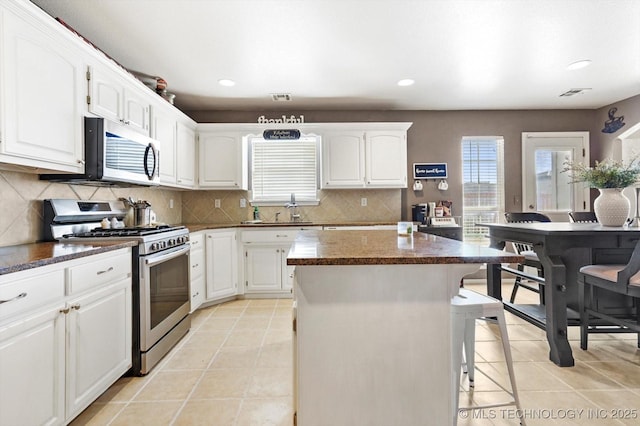 kitchen featuring a kitchen island, white cabinetry, a breakfast bar area, decorative backsplash, and stainless steel appliances