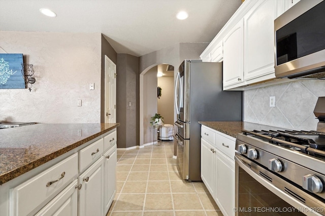 kitchen with light tile patterned floors, white cabinetry, backsplash, stainless steel appliances, and dark stone counters