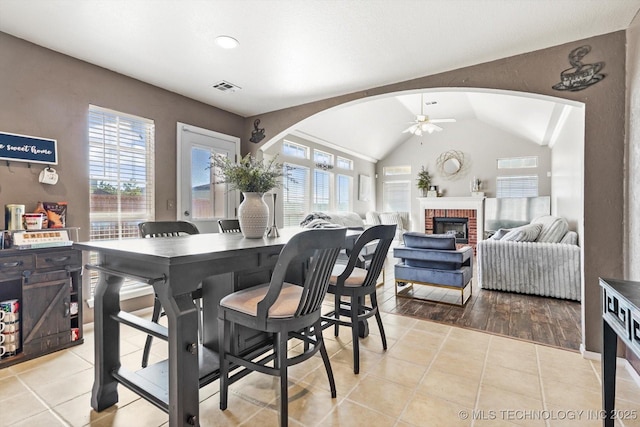 dining area with lofted ceiling, a brick fireplace, light tile patterned floors, and ceiling fan