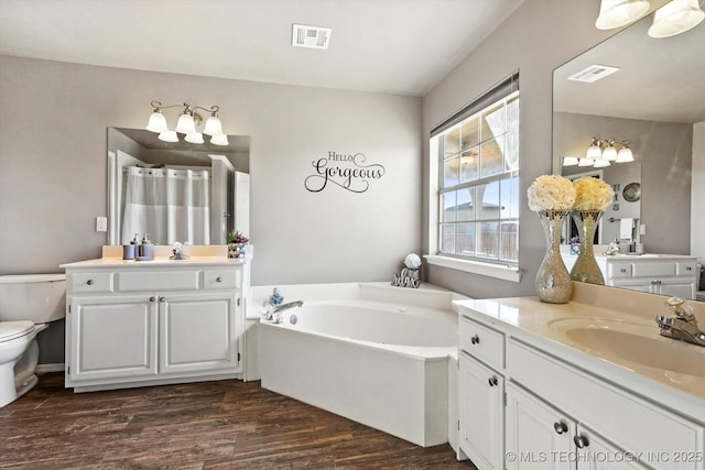 bathroom with wood-type flooring, toilet, vanity, and a tub to relax in