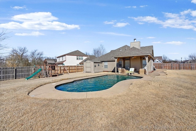 view of pool with a storage unit, a playground, a fenced backyard, an outbuilding, and a fenced in pool