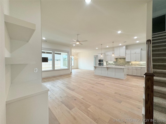 kitchen with decorative light fixtures, light wood-type flooring, an island with sink, decorative backsplash, and white cabinets