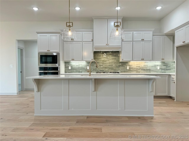 kitchen with stainless steel microwave, an island with sink, pendant lighting, and white cabinets