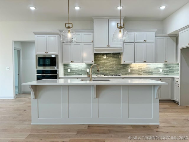 kitchen with hanging light fixtures, appliances with stainless steel finishes, a kitchen island with sink, and sink